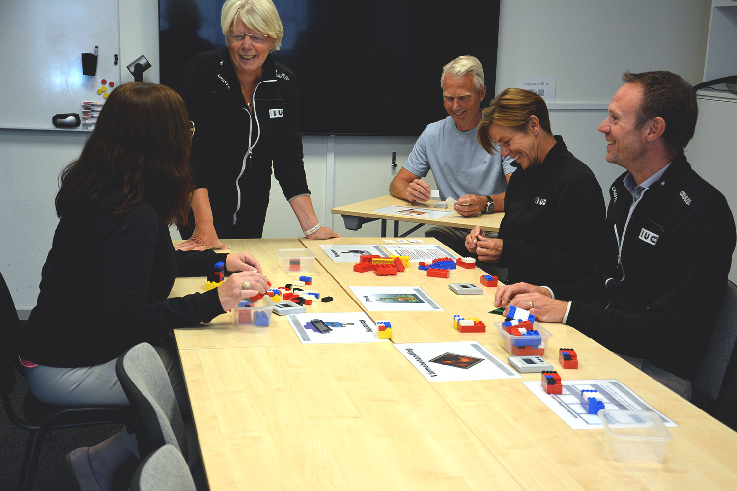 Grupp vuxna deltar i en utbildning med övningar där de använder färgglada byggklossar vid ett bord.