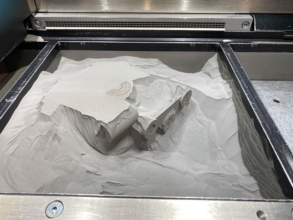 3D-utskrift i metall med pulverbädd – komponenten håller på att framträda ur det kompakta pulverlagret.