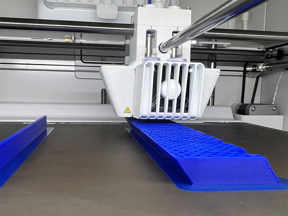 Ultimaker-skrivare i färd med att skriva ut ett blått, strukturerat 3D-objekt i verkstadsmiljö.