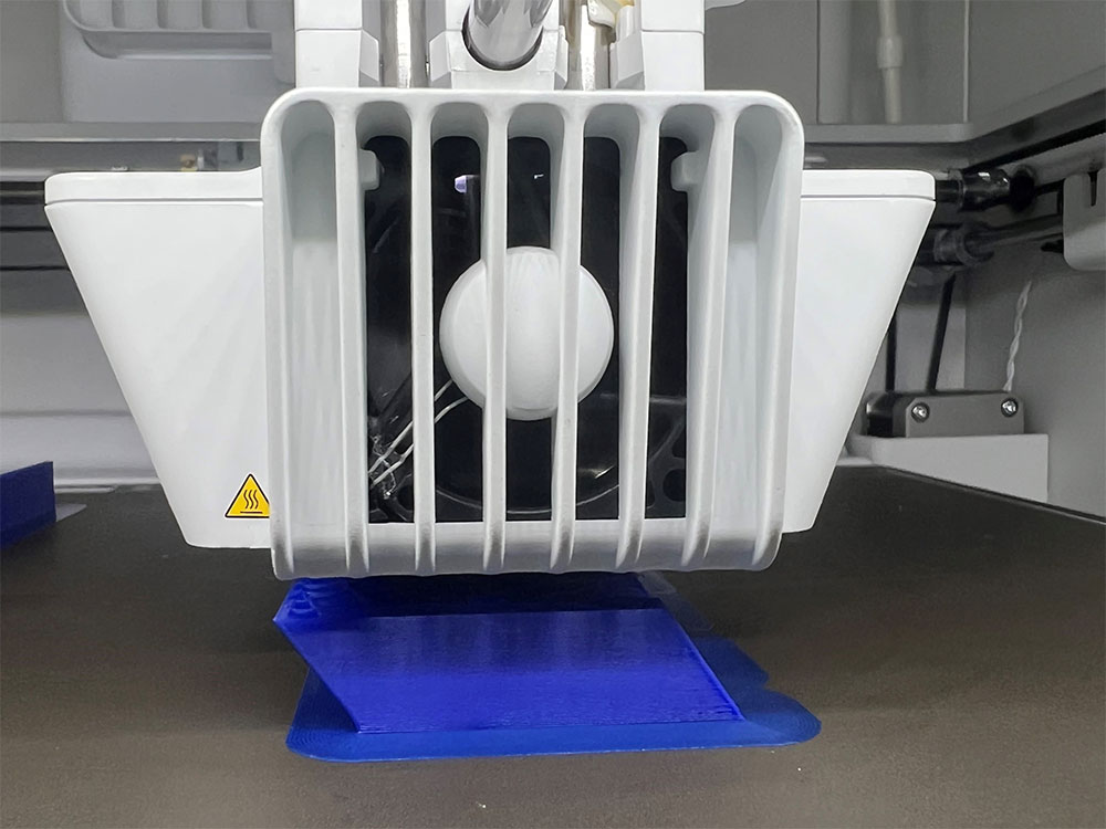 Närbild av Ultimaker 3D-skrivare som skriver ut blå plastkomponent på byggplattan.