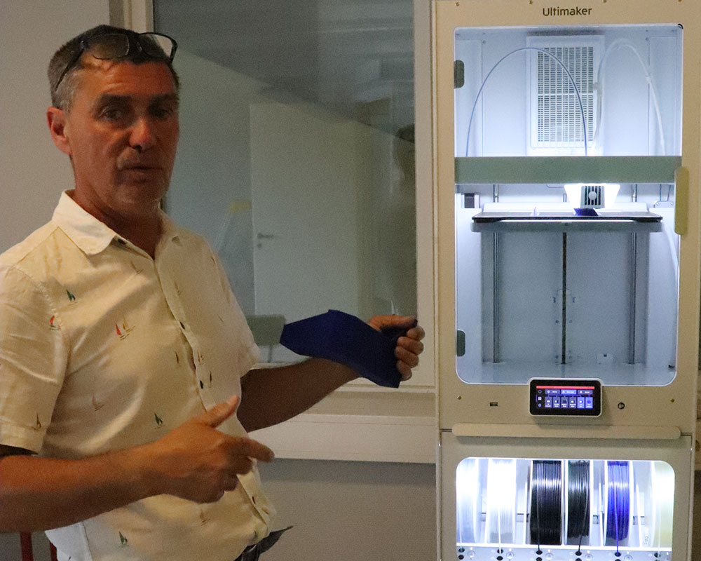 Man visar en blå 3D-utskriven komponent vid en Ultimaker 3D-skrivare i modern labbmiljö.