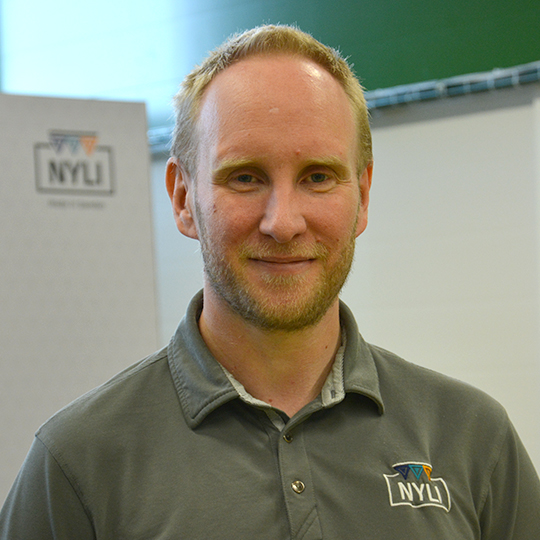 Andreas Thorn från NYLI poserar leende i profiltröja med företagets logotyp i bakgrunden.