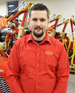 En man i röd skjorta med Kranman-logga står framför monterade skogsmaskiner i en verkstadsmiljö.