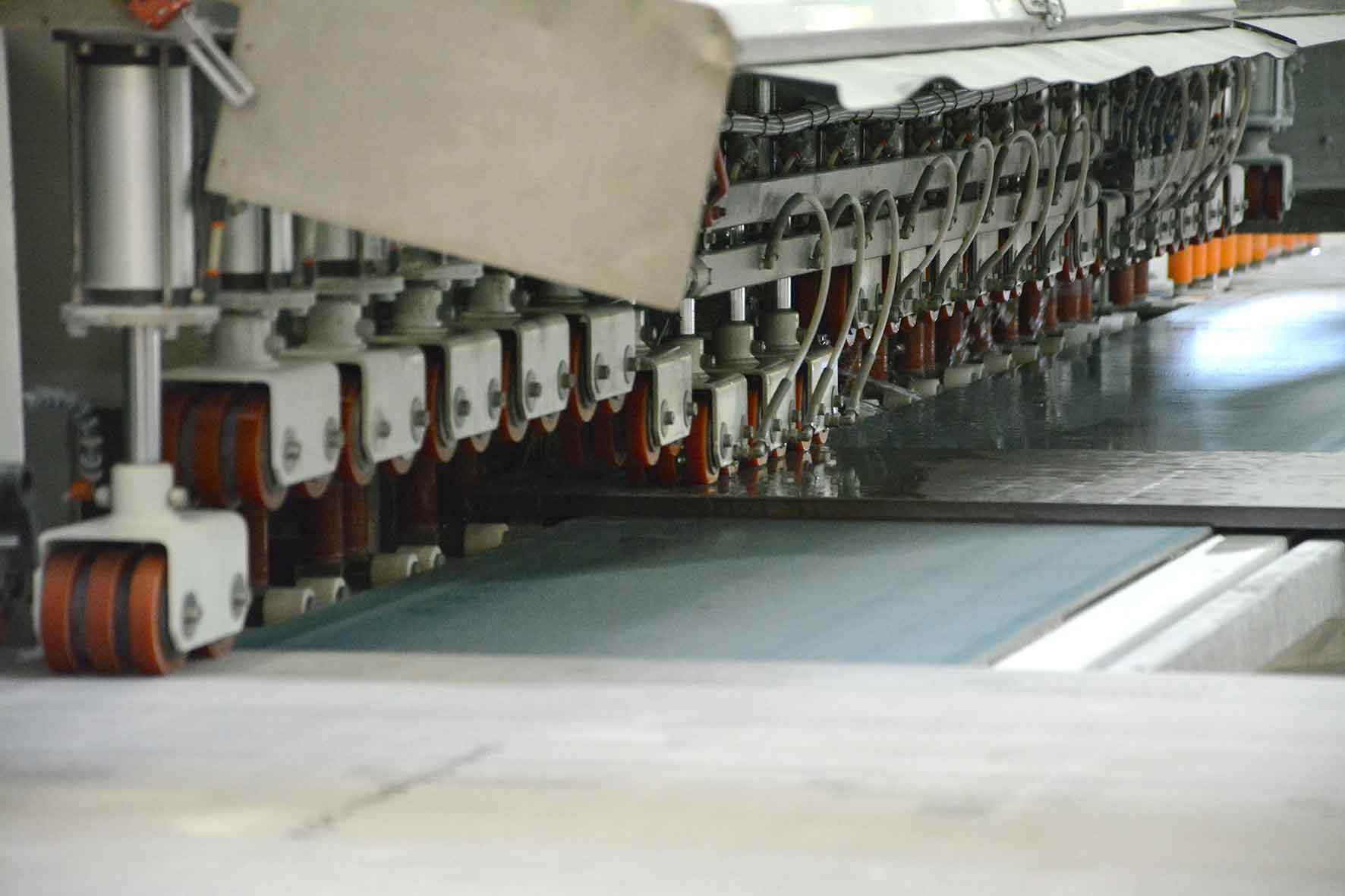 Automatisk maskin kantslipar en stor stenplatta i industriell miljö.