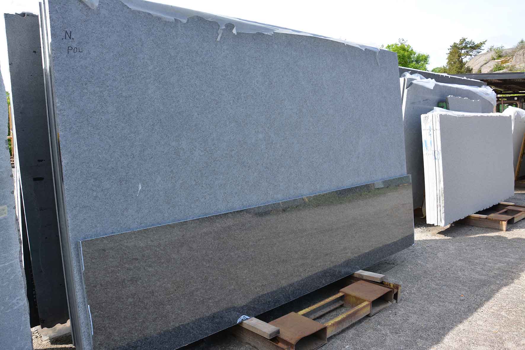 Polerad granitskiva står lutad mot råmaterial i utomhuslager.