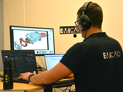 Ingenjör på EmiCAD arbetar vid två skärmar med CAD-programvara, bär headset.