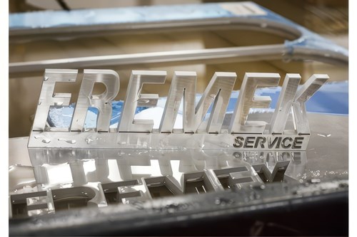 Glansig metallskylt med texten "FREMEK SERVICE" speglas i en blank yta.
