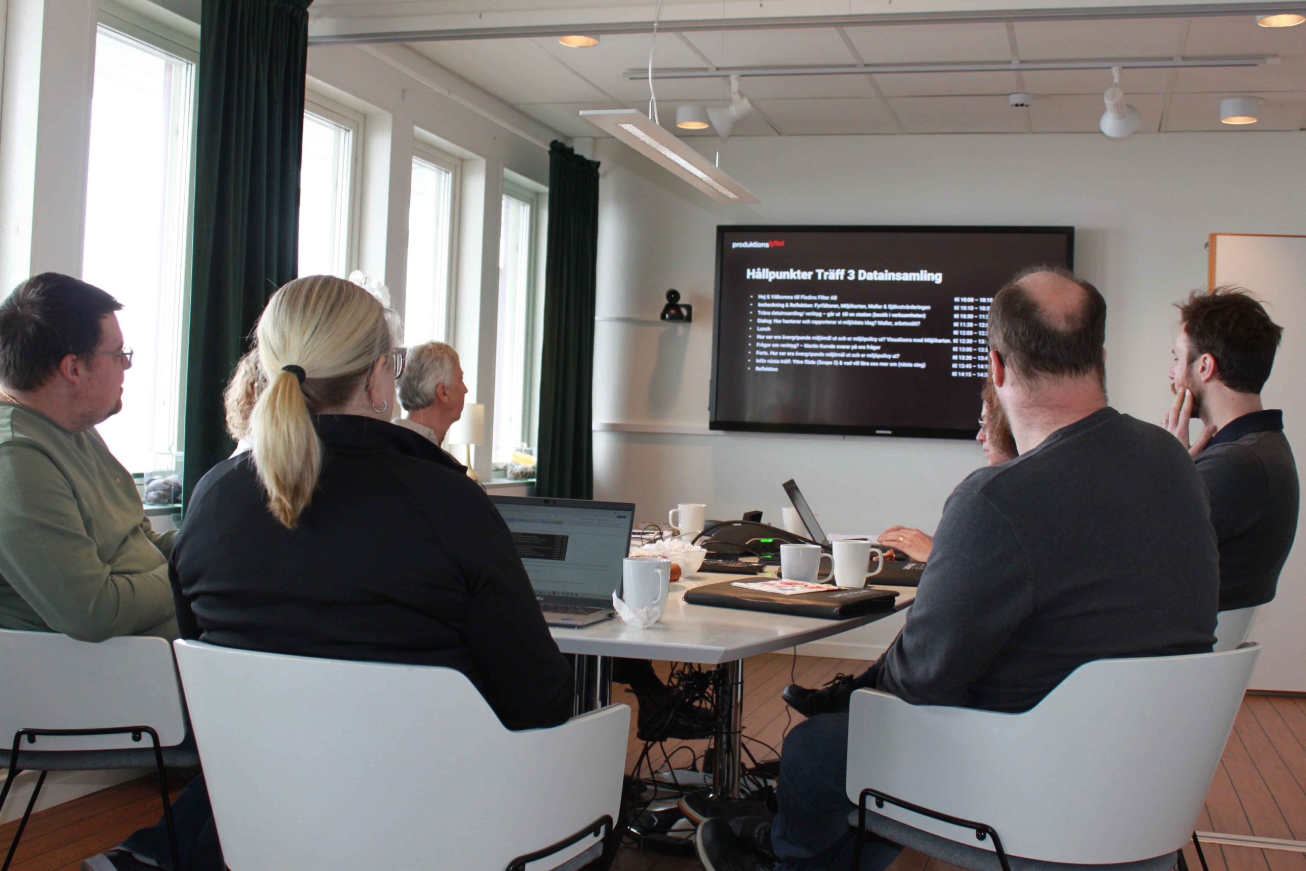 Grupp i mötesrum tittar på presentation om datainsamling på storbildsskärm.