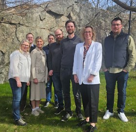 Grupp personer poserar tillsammans utomhus framför en bergvägg i vårsolen.