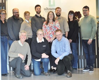 Leende grupp poserar inomhus framför skylt med logotypen "Ultramare".