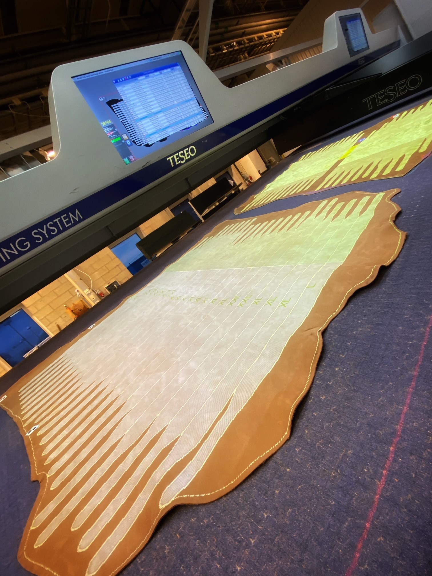 Industrimaskin med laserskurna mönster i läder under skärningsprocess.