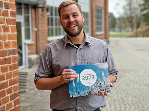 Leende man håller i hållbarhetsredovisning 2023 från Ultramare, framför tegelbyggnad.