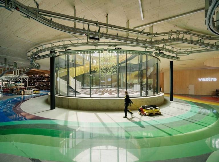 Modern interiör från Vestre-fabriken The Plus, med glasat atrium, färgglad golvdesign och automatiserad miljövänlig produktion.