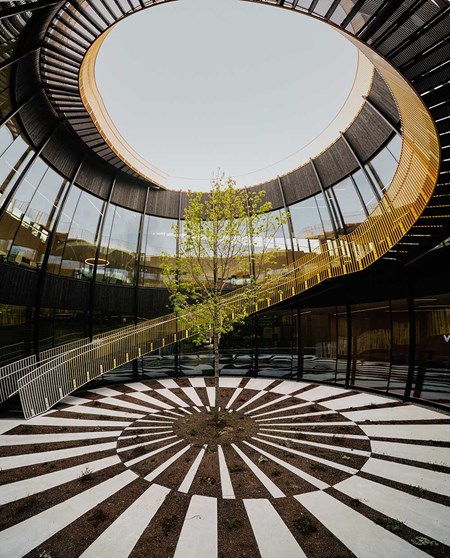 Centralt atrium med träd i fokus, spiralformad trappa och öppen takkupol i Vestres fabrik The Plus.