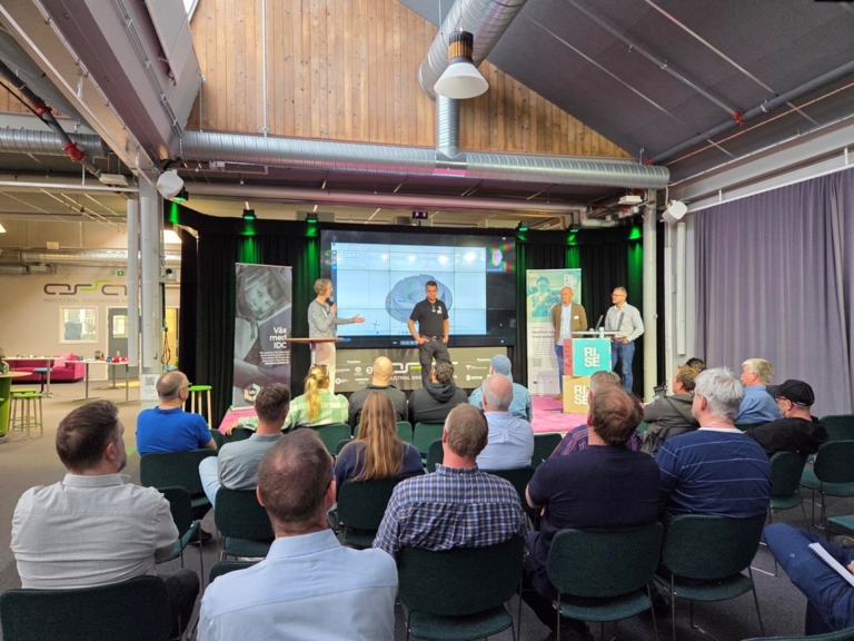 Talare och panel på scen under 3D-Actio eventet på ASSAR i Skövde, med stor presentation på skärmen bakom.
