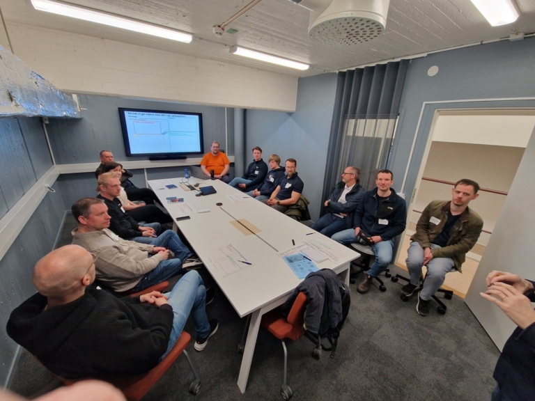 Grupp personer sitter samlade runt ett konferensbord under ett studiebesök i 3D-Action på Volvo Torslanda