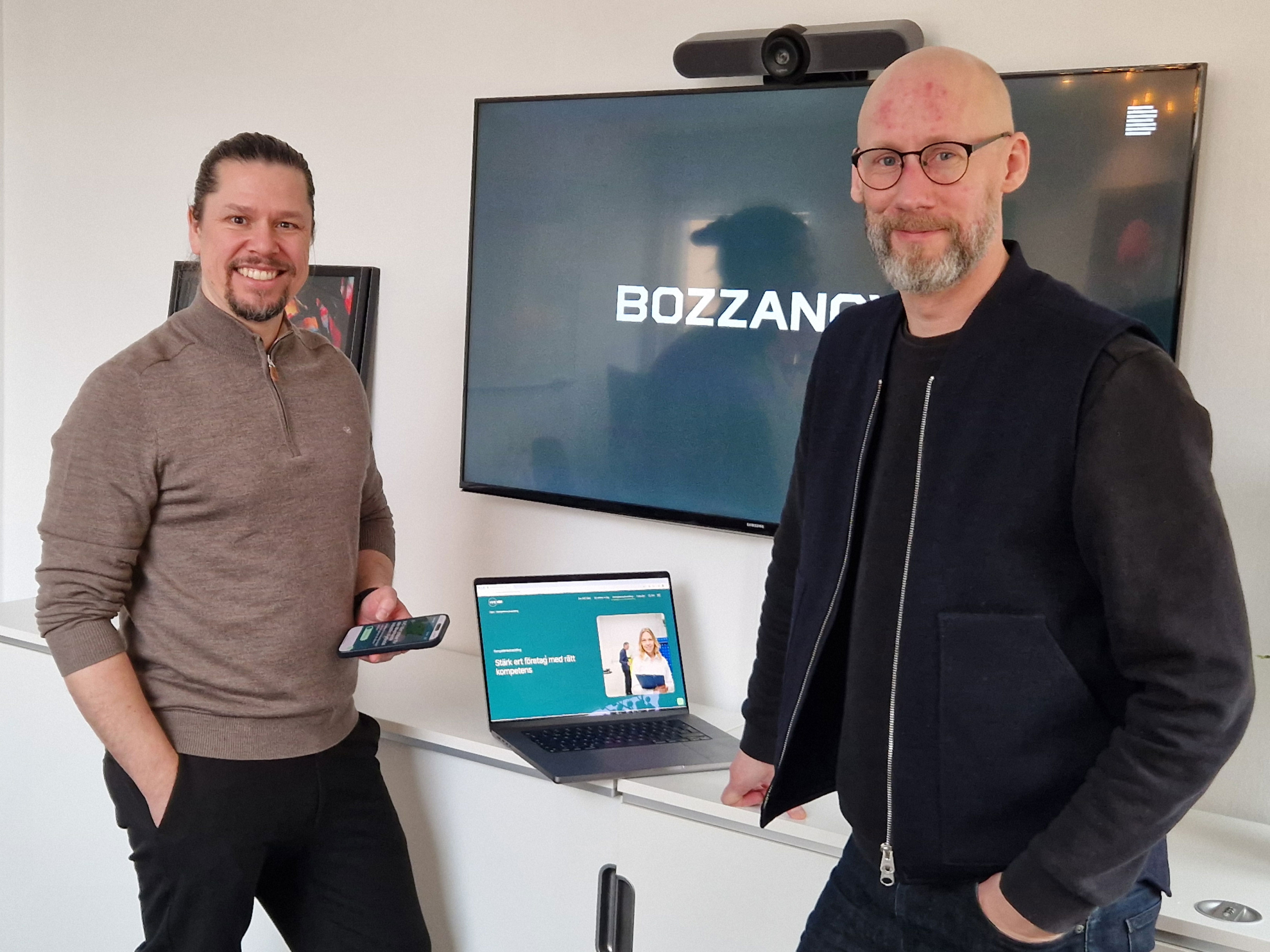 Två personer står i ett mötesrum framför en skärm med Bozzanova-logotypen; en laptop är uppställd på ett bord. Ny webbplats med tillgänglighet i fokus.