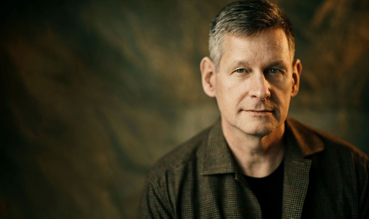 Porträtt av Robert Karjel som ser in i kameran, mot en suddig bakgrund i varma toner. Föreläsning Bli någon att räkna med.